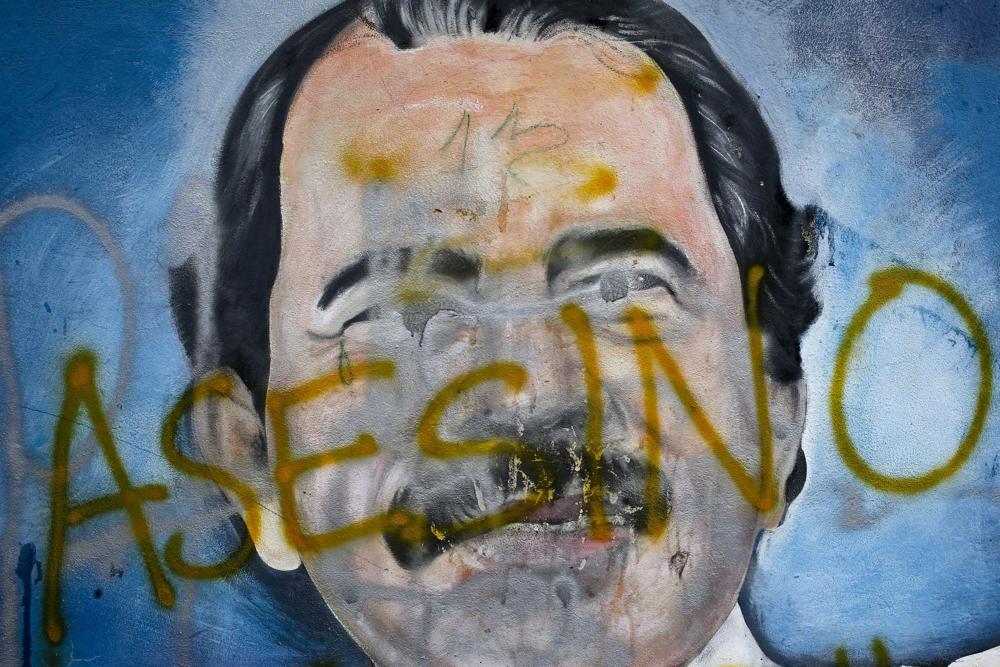 FILE - The Spanish word for Murderer covers a mural of Nicaragua's President Daniel Ortega, as part of anti-government protests demanding his resignation in Managua, Nicaragua, May 26, 2018. Four months before scheduled 2022 municipal elections, Nicaraguan riot police have taken over the city halls of five municipalities that had been in the hands of an opposition party. (AP Photo/Esteban Felix, File)