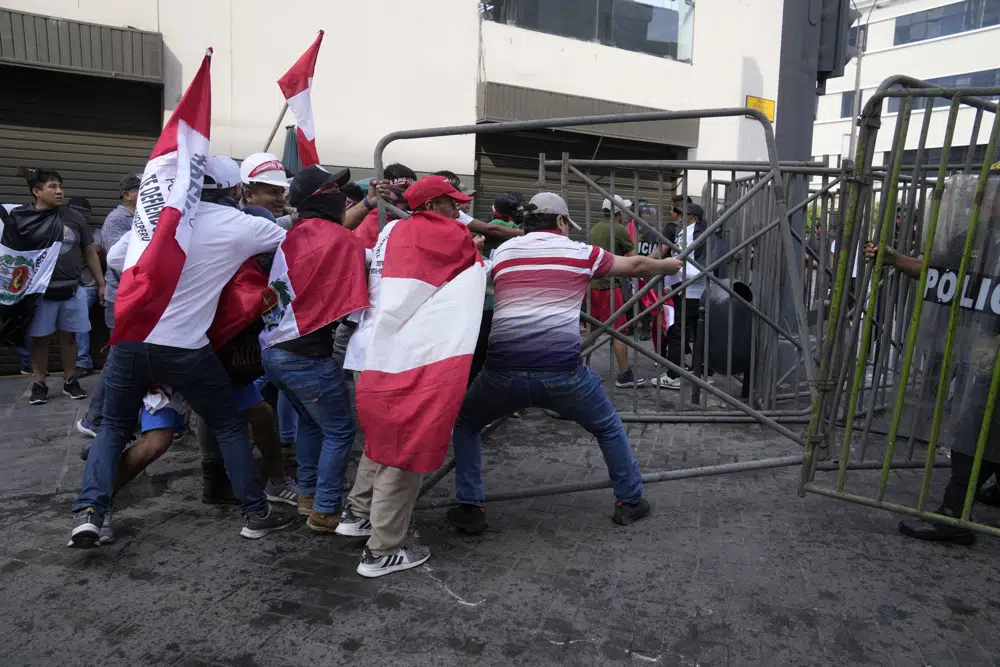 Manifestantes opositores que viajaron a la capital desde otras partes del país para marchar contra la presidenta peruana Dina Boluarte derriban una barricada de la policía durante los enfrentamientos en Lima, Perú, el jueves 19 de enero de 2023. Las protestas buscan un adelanto electoral inmediato, la renuncia de Boluarte, la liberación del presidente destituido Pedro Castillo y justicia por los al menos 48 manifestantes muertos en enfrentamientos con la policía. (AP Foto/Martín Mejía)