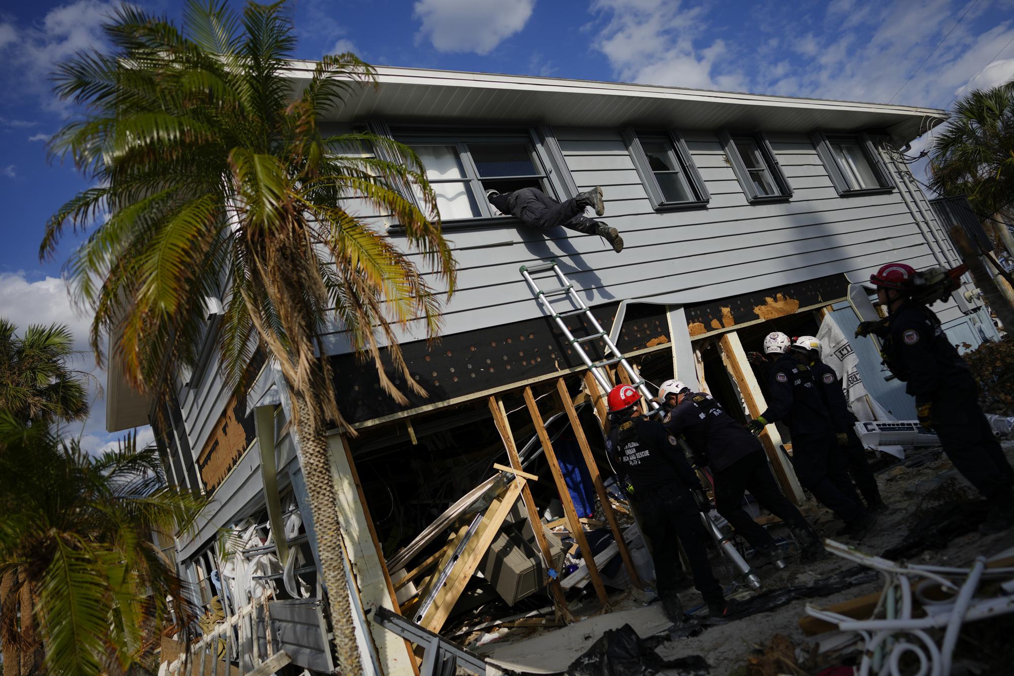 Los miembros de Florida Task Force 2 de búsqueda y rescate urbano obtienen acceso a una casa a través de una ventana superior rota para confirmar que la casa está libre de personas y restos humanos, una semana después del paso del huracán Ian, en Fort Myers Beach, Florida, el 5 de octubre de 2022. (Foto AP/Rebecca Blackwell)