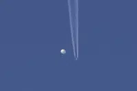 In this photo provided by Brian Branch, a large balloon drifts above the Kingstown, N.C. area, with an airplane and its contrail seen below it. The United States says it is a Chinese spy balloon moving east over America at an altitude of about 60,000 feet (18,600 meters), but China insists the balloon is just an errant civilian airshipused mainly for meteorological research that went off course due to winds and has only limited “self-steering” capabilities. (Brian Branch via AP)