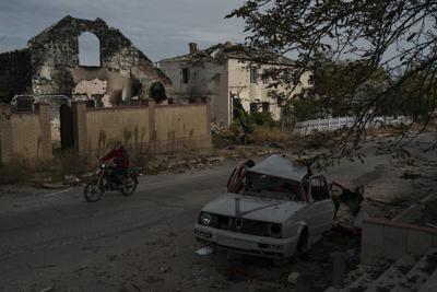 Un hombre pasa en motocicleta junto a un auto destruido en la localidad de Velyka Oleksandrivka, recuperada por el ejército ucraniano, en Ucrania, el 12 de octubre de 2022. (AP Foto/Leo Correa)