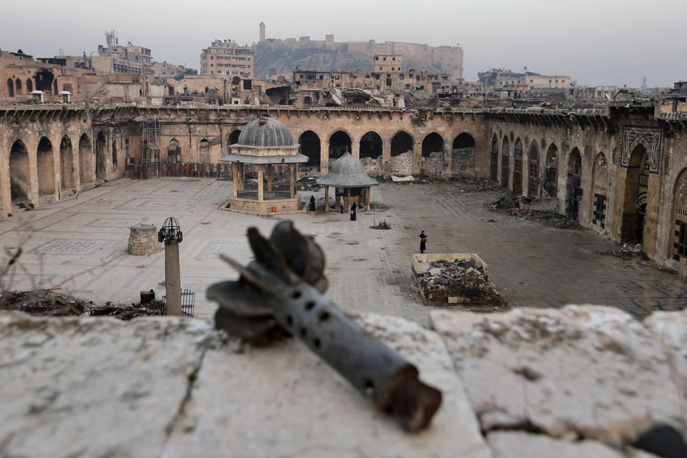 FILE - A mortar shall is seen in the foreground as people visit the heavily damaged Grand Umayyad mosque while the Aleppo citadel is seen in the background, in the old city of Aleppo, Syria, Thursday, Jan. 19, 2017. For years, the people of Aleppo bore the brunt of bombardment and fighting when their city, once Syria's largest and most cosmopolitan, was one of the civil war's fiercest battle zones. Even that didn't prepare them for the new devastation and terror wreaked by this week's earthquake. (AP Photo/Hassan Ammar, File)