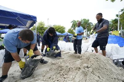 Operarios municipales llenan sacos de arena en un puesto de reparto a residentes antes de la llegada de las lluvias asociadas a la tormenta tropical Fred, el 13 de agosto de 2021, en Grapeland Park, Miami. (AP Foto/Wilfredo Lee)