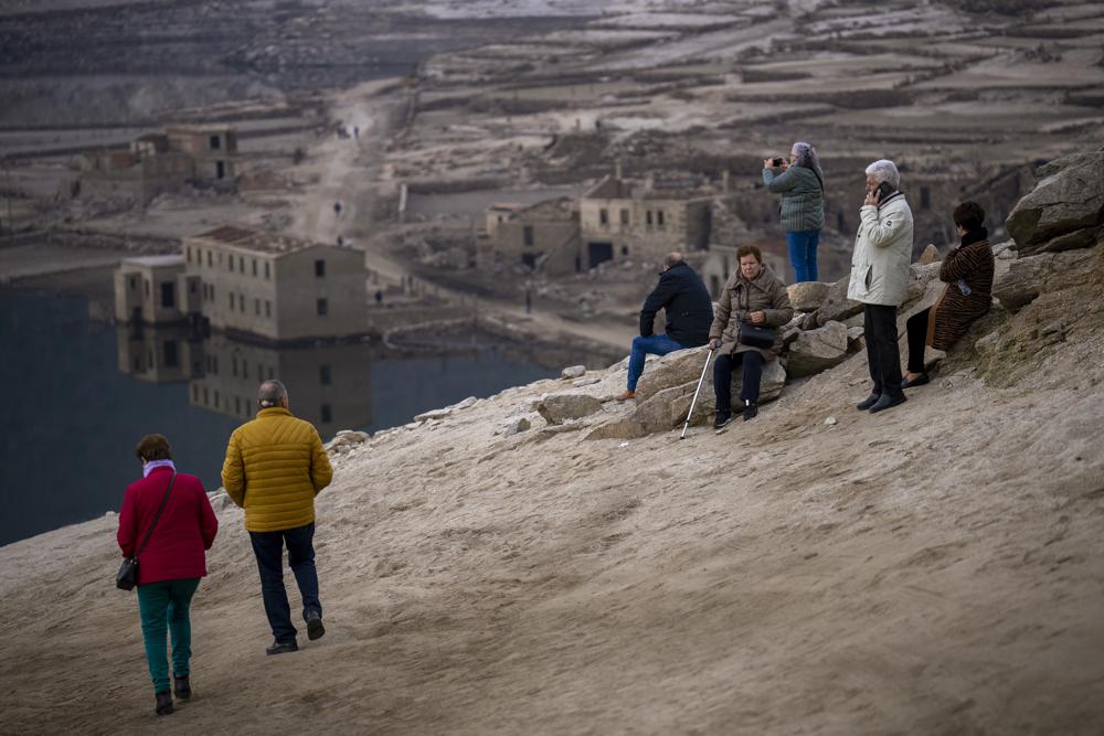 Visitantes miran al antiguo pueblo de Aceredo, visible debido a la sequía, en el embalse de Lindoso, en el noroeste de España, el sábado 12 de febrero de 2022. Los tejados asomando en el agua se han convertido en una escena habitual en verano en el embalse de Lindoso, en el noroeste de España. En años especialmente secos aparecían partes del antiguo pueblo, sumergido hace tres décadas cuando una presa hidroeléctrica inundó el valle. Pero nunca había reaparecido el pueblo entero en pleno invierno. (AP Foto/Emilio Morenatti)