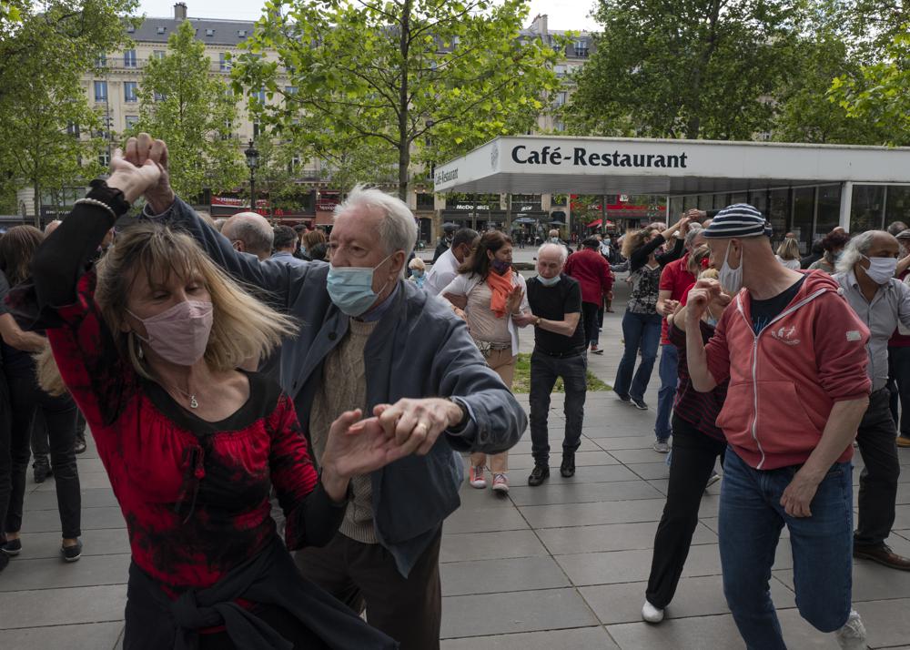 FILE - In this May 23, 2021, file photo, a couple with protective masks on dance at Republic square in Paris. Coronavirus infections, hospitalizations and deaths are plummeting across much of Europe. Vaccination rates are accelerating, and with them, the promise of summer vacations. (AP Photo/Rafael Yaghobzadeh, File)