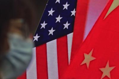 ARCHIVO_ En esta foto del 22 de febrero del 2021, una mujer está sentada junto a una pantalla que muestra banderas de Estados Unidos y China mientras escucha un discurso en el Lating Forum en el Ministerio de Relaciones Exteriores en Beijing.  Altos diplomáticos de Estados Unidos y China al perecer se enfrascaron el 11 de junio en otro agudo intercambio, con Beijing diciendo que le dijo a Washington que dejase de interferir en sus asuntos internos y acusando a los estadounidenses de politizar la búsqueda del origen del COVID-19. (AP Foto/Andy Wong)
