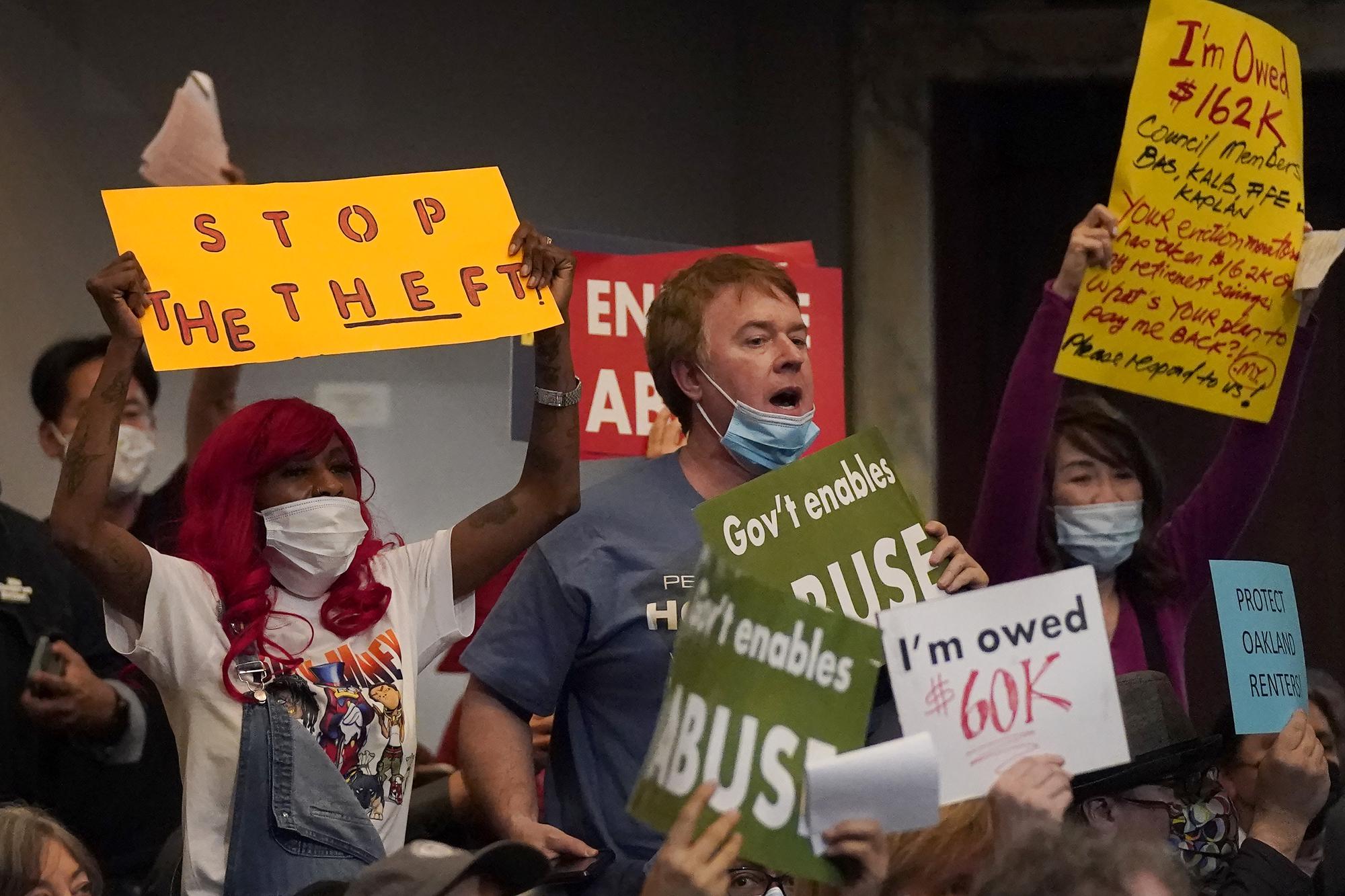 Chris Moore, middle, of the East Bay Rental Housing Association board, holds up signs with others during a Oakland City Council special community and economic development committee at City Hall in Oakland, Calif., Tuesday, April 11, 2023. Some landlords have gone without rental income for more than three years after Oakland, California approved an eviction moratorium in March 2020. (AP Photo/Jeff Chiu)