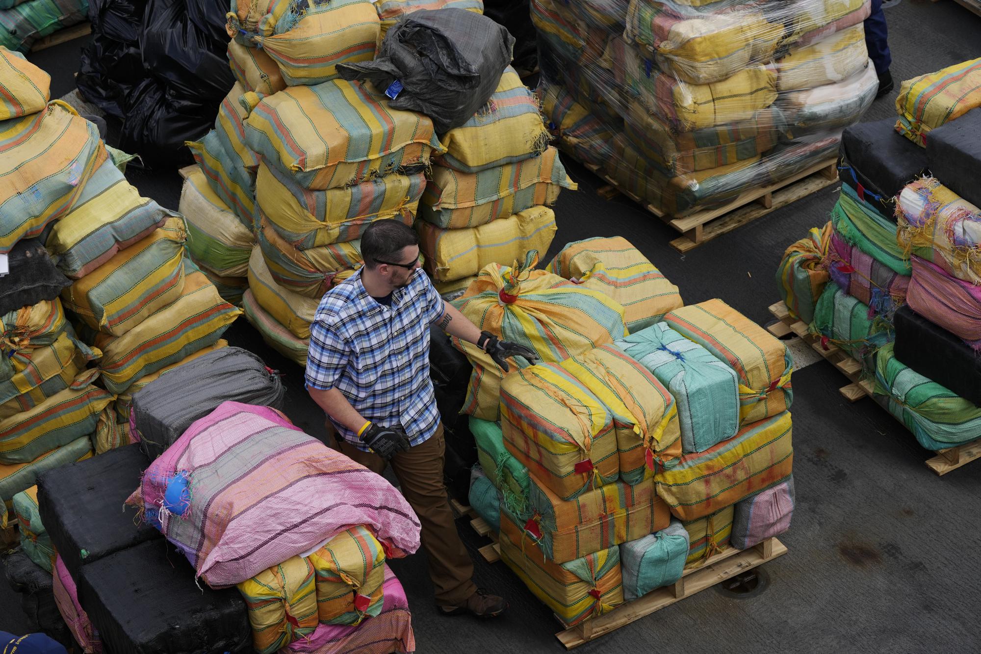 FILE - A man walks amidst bundles of seized cocaine and marijuana, as the U.S. Coast Guard and other agencies prepare to unload more than one billion dollars worth of seized drugs from Coast Guard Cutter James at Port Everglades, Thursday, Feb. 17, 2022, in Fort Lauderdale, Fla. The Coast Guard said the haul included approximately 54,500 pounds of cocaine and 15,800 pounds of marijuana from multiple interdictions in the Caribbean Sea and the eastern Pacific. (AP Photo/Rebecca Blackwell, File)