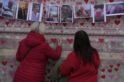FILE - Family members write a message to two sisters who died of COVID on the National Covid Memorial wall in London, Tuesday, March 29, 2022. Latest figures from Britain's statistics agency show the prevalence of COVID-19 in the U.K. has reached record levels, with about 1 in 13 people estimated to be infected with the virus in the past week. Some 4.9 million people were estimated to have the virus in the week ending March 26, up from 4.3 million recorded in the previous week, the Office for National Statistics said Friday, April 1, 2022.  (AP Photo/Alastair Grant, File)