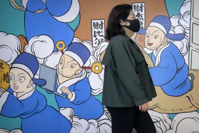 Una mujer, con mascarilla por la pandemia del coronavirus, pasa por delante de un mural, en Beijing, el 22 de abril de 2022. (AP Foto/Mark Schiefelbein)