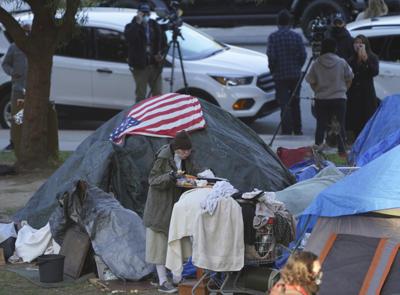 ARCHIVO - En esta fotografía de archivo del 24 de marzo de 2021, una mujer come afuera de su tienda de campaña en el campamento de personas sin casa en Echo Park Lake, en Los Ángeles. (AP Foto/Damian Dovarganes, archivo)