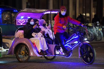 People ride in a bike taxi near Leicester Square in London, Thursday, Dec. 30, 2021. British Prime Minister Boris Johnson has resisted implementing new restrictions on business and social interactions during the holiday season, instead emphasizing an expanded vaccine booster program to control the spread of omicron. (Jonathan Brady/PA via AP)