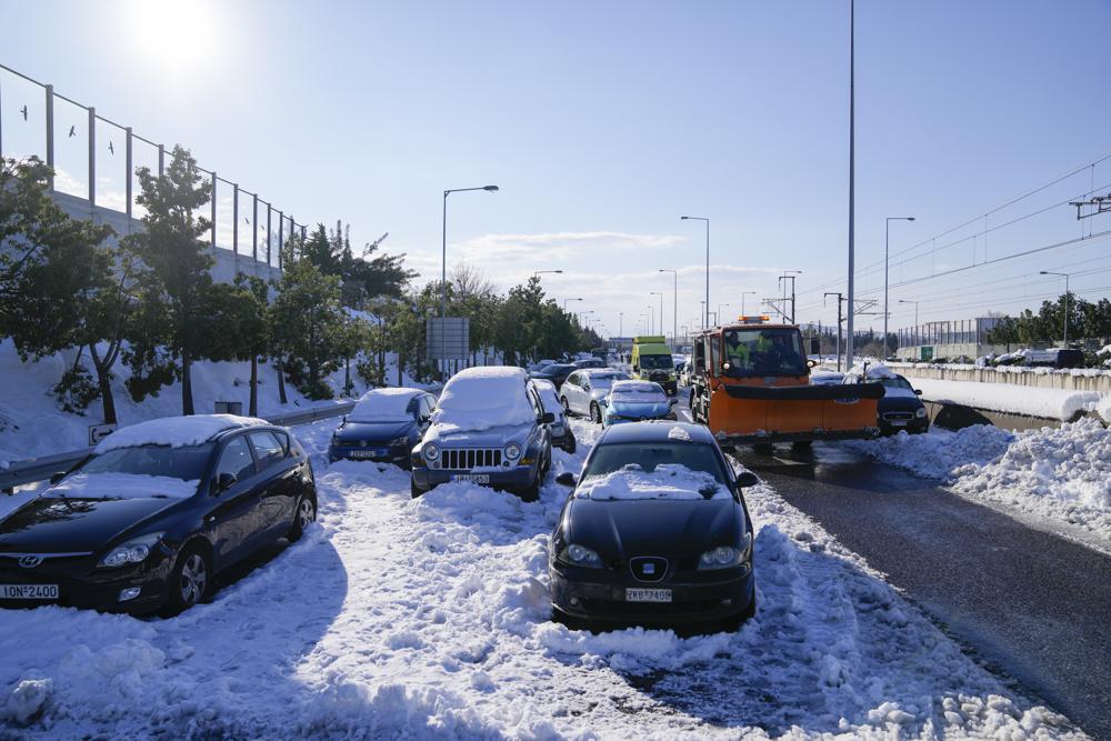 Una máquina quitanieves pasa junto a vehículos abandonados atrapados en la nieve en la autopista Attiki Odos, luego de la fuerte nevada del martes en Atenas, el miércoles 26 de enero de 2022. (Foto AP/Thanassis Stavrakis)