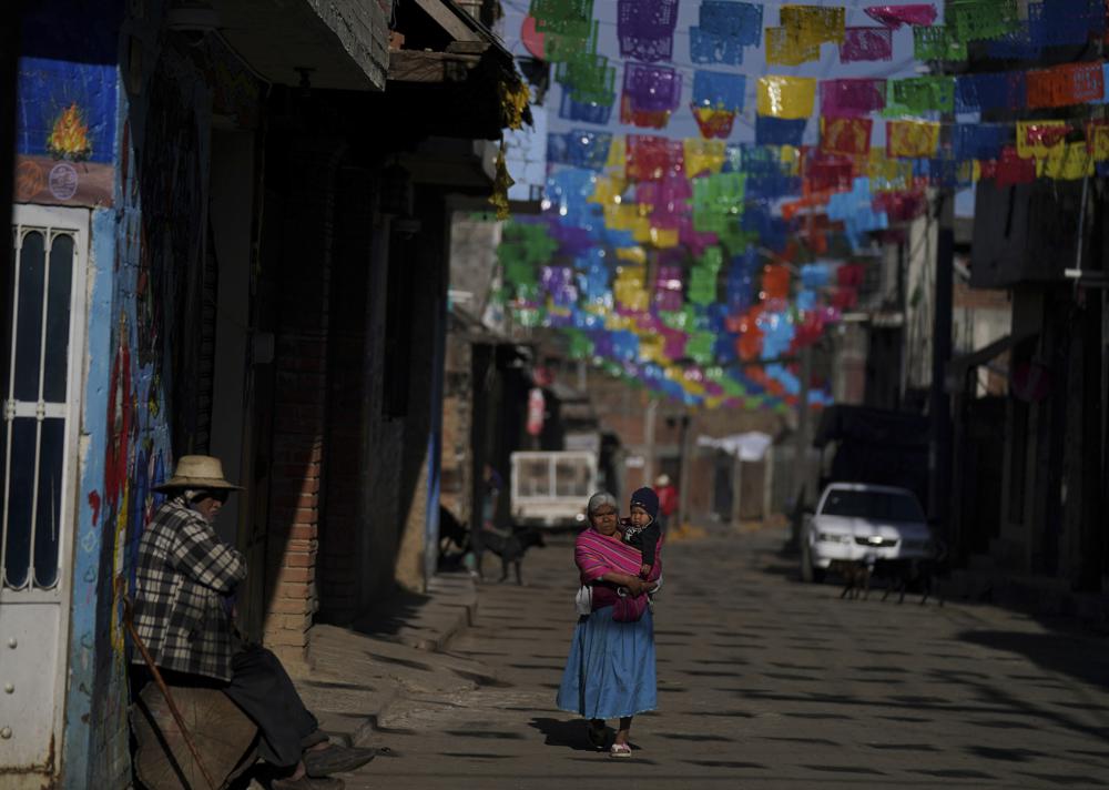 Vecinos en una calle decorada con papel picado, en la comunidad indígena puerpecha de Comachuén, México, el miércoles 19 de enero de 2022. En algunos lugares del México rural, las remesas mantienen con vida a muchos poblados. (AP Foto/Fernando Llano)