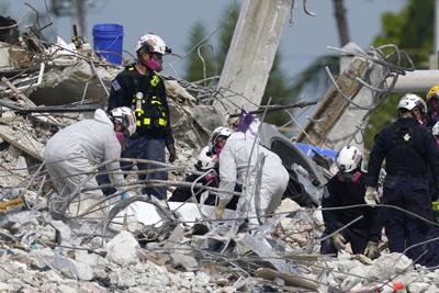 Rescatistas levantan una lona que contiene restos humanos recogidos en el sitio del edificio residencial derrumbado Champlain Towers South en Surfside, Florida, 5 de julio de 2021. (AP Foto/Lynne Sladky)