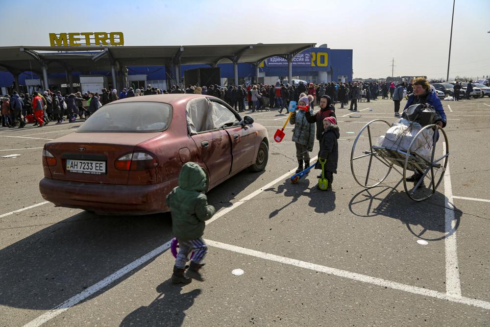 Local residents gather near a supermarket to get free food and water on the territory which is under the Government of the Donetsk People's Republic control, on the outskirts of Mariupol, Ukraine, Thursday, March 24, 2022. (AP Photo/Alexei Alexandrov)