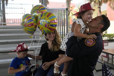 El capitán Eric Hernandez alza a su hija Isabella, de 3 años, ante la mirada de su esposa Yaimara y su hijo Eric, de 4 años. Los miembros del equipo de búsqueda y rescate de los bomberos de Miami-Dade se reunieron de nuevo con sus familias tras semanas de trabajar en la pila de escombros que quedó del edificio desplomado Champlain Towers South, el viernes 23 de julio de 2021, en Doral, Florida. (AP Foto/Rebecca Blackwell)