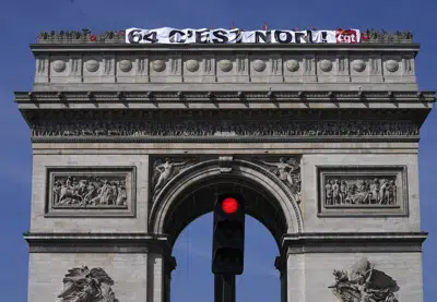 Sindicalistas despliegan una pancarta con la leyenda "64 es no" en lo alto del Arco de Triunfo, París, miércoles 5 de abril de 2023. Los sindicatos convocaron a grandes movilizaciones para el jueves 6 de abril al fracasar las conversaciones con el primer ministro en busca de un acuerdo sobre la elevación de la edad jubilatoria de 62 a 64 años. (AP Foto/Michel Euler)