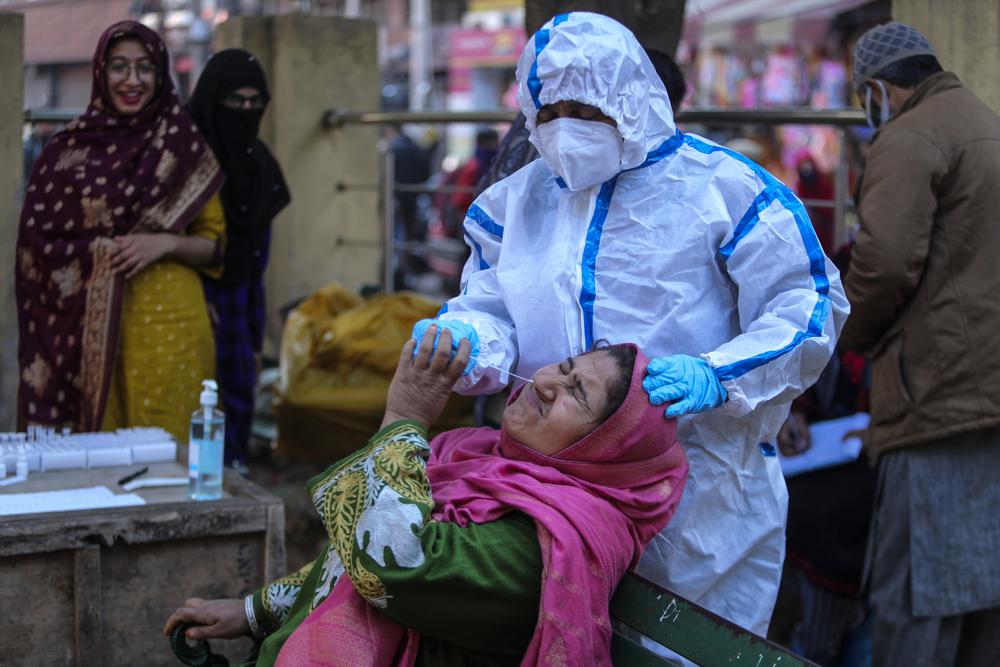 A health worker collects a swab sample of a woman to test for COVID-19 at a market in Jammu, India, Wednesday, Dec.29, 2021. In India, which has been getting back to normal after a devastating COVID-19 outbreak earlier this year, omicron is once again raising fears, with more than 700 cases reported in the country of nearly 1.4 billion people. (AP Photo/Channi Anand)