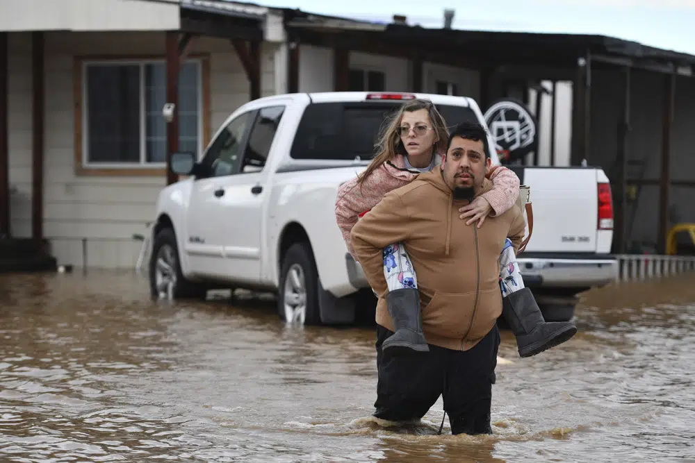 Ryan Orosco, of Brentwood, carries his wife Amanda Orosco, from their flooded home on Bixler Road in Brentwood, Calif., on Monday, Jan. 16, 2023. The last in a three-week series of major winter storms is churning through California. (Jose Carlos Fajardo/Bay Area News Group via AP)