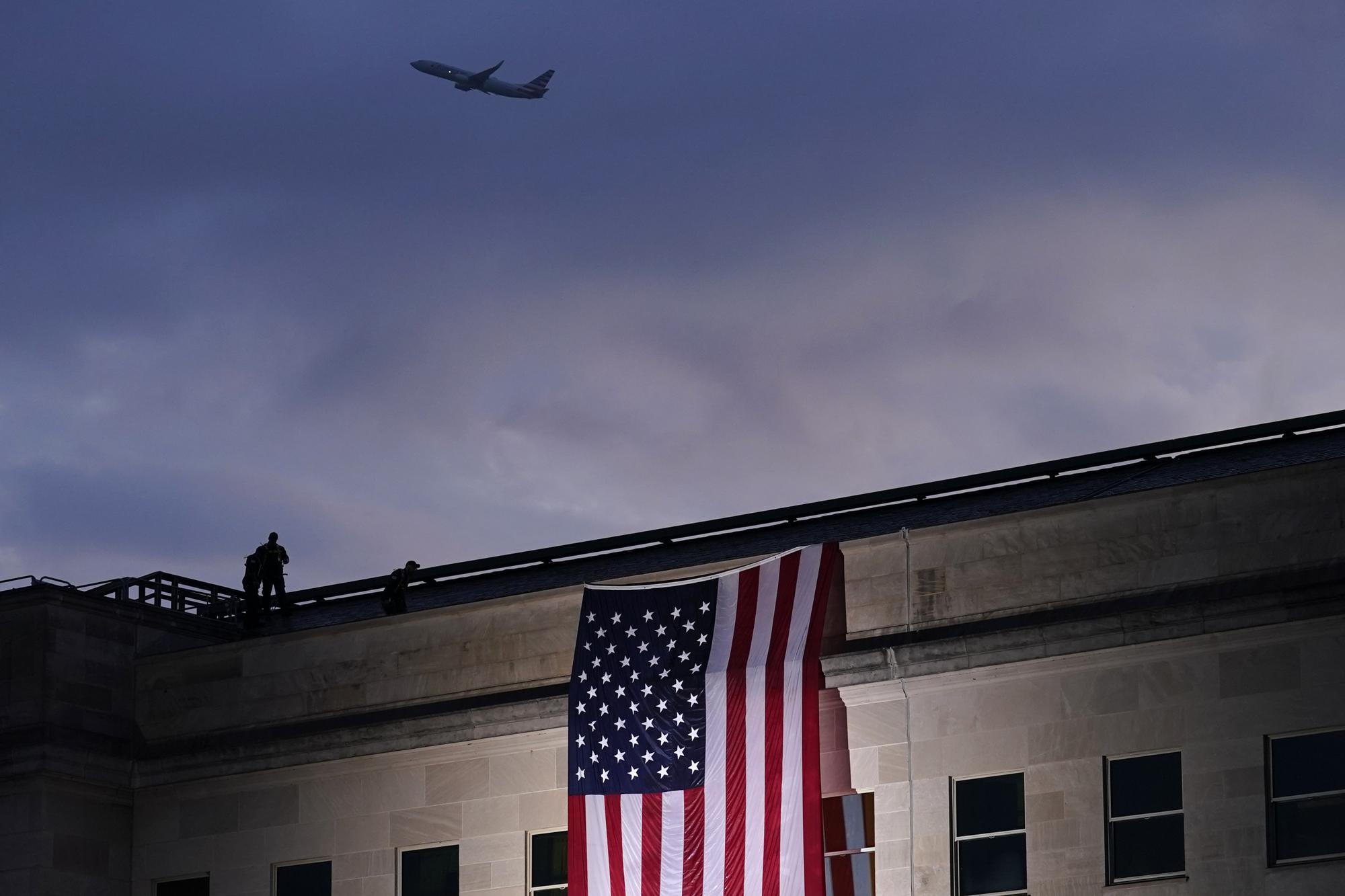 FILE - In this Friday, Sept. 11, 2020 file photo, a plane takes off from Washington Reagan National Airport as a large U.S. flag is unfurled at the Pentagon ahead of ceremonies at the National 9/11 Pentagon Memorial to honor the 184 people killed in the 2001 terrorist attack on the Pentagon, in Washington, Friday, Sept. 11, 2020. (AP Photo/J. Scott Applewhite, File)