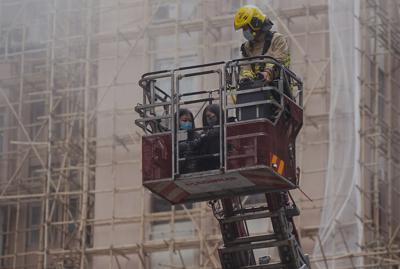 Dos mujeres son rescatadas de un incendio por un bombero en una grúa ante el World Trade Centre, en el popular distrito comercial de Causeway Bay, Hong Kong, el miércoles 15 de diciembre de 2021. (AP Foto)