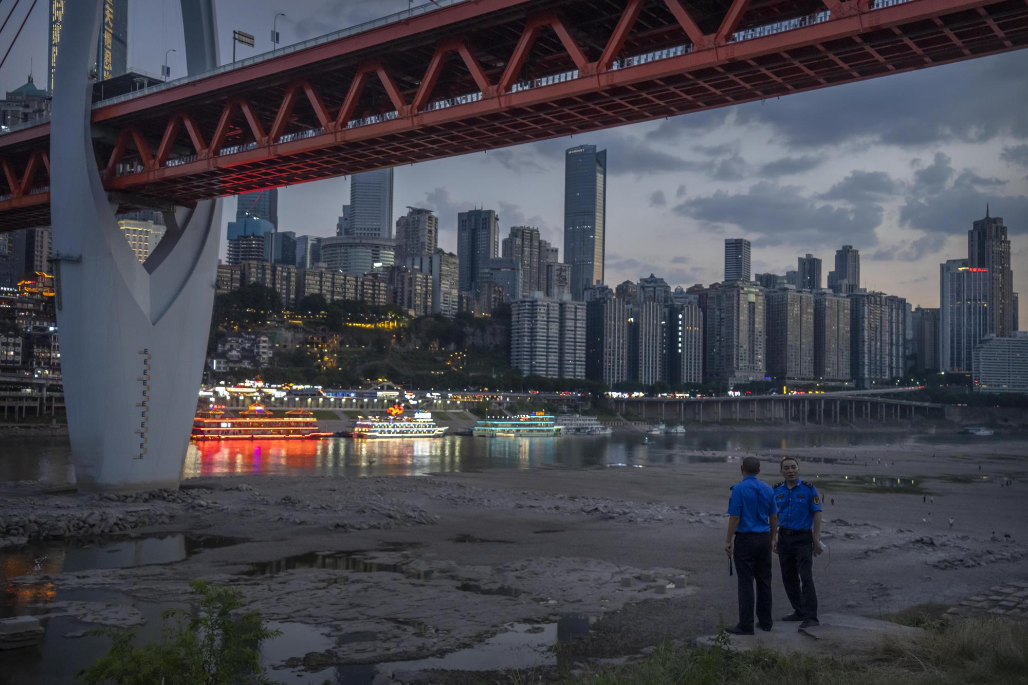 Security officers stand on a hillside after clearing away visitors from the dry riverbed of the Jialing River, a tributary of the Yangtze, in southwestern China's Chongqing Municipality, Saturday, Aug. 20, 2022. The very landscape of Chongqing, a megacity that also takes in surrounding farmland and steep and picturesque mountains, has been transformed by an unusually long and intense heat wave and an accompanying drought. (AP Photo/Mark Schiefelbein)