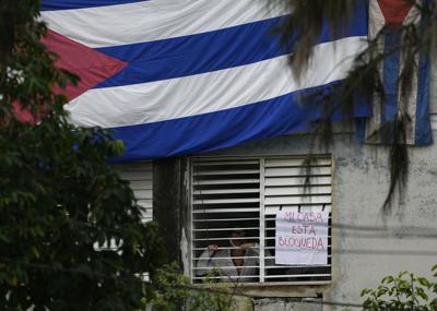 Yunior García Aguilera, dramaturgo y uno de los organizadores de una marcha de protesta el 15 de noviembre, aparece junto a un letrero que dice "Mi casa está bloqueada", que colgó en una ventana de su casa, en La Habana, Cuba, el domingo de noviembre. 14, 2021. Se han colgado banderas cubanas en las ventanas y puertas de la casa de García Aguilera para evitar que se comunique con el exterior. (Foto AP/Ramón Epinosa)