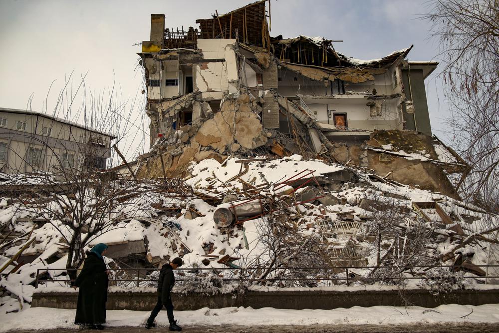 La gente pasa frente a un edificio derrumbado en Malatya, Turquía, el martes 7 de febrero de 2023. Los equipos de búsqueda y la ayuda llegan a Turquía y Siria mientras los rescatistas trabajan en temperaturas bajo cero excavando entre los restos de los edificios arrasados ​​por un terremoto de magnitud 7,8.  (Foto AP/Emrah Gurel)