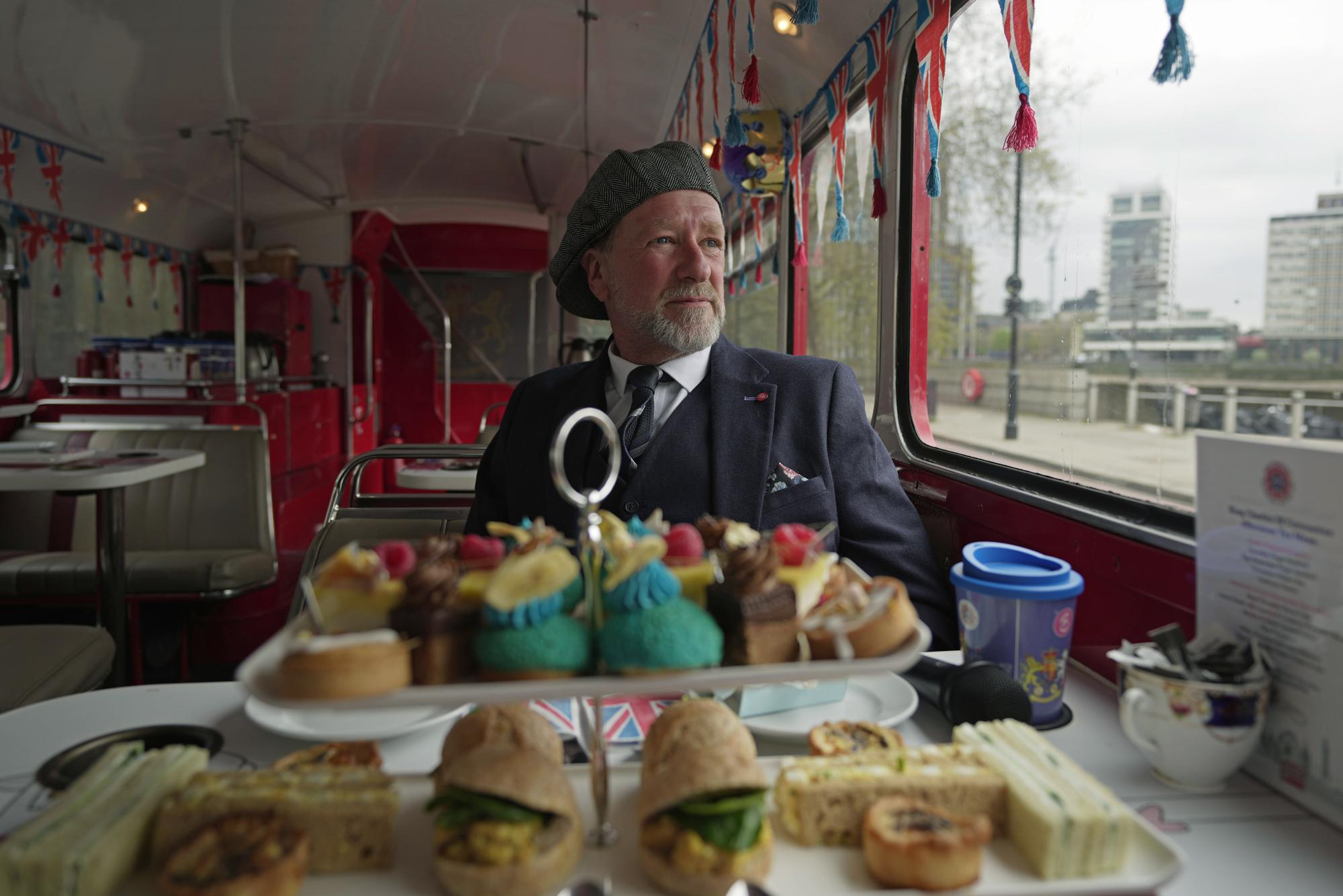 Tourist guide Mel Adams sits on a bus, part of the Coronation Tour Bus route, in London, Monday, April 24, 2023. The May 6 coronation is luring royal fans and far-flung visitors fascinated by the ceremonial spectacle — and drama — of the monarchy and eager to experience a piece of British history. Tour companies, shops and restaurants are rolling out the red carpet, whether it's a decked-out bus tour of London's top sights boasting high tea or merchandise running from regal to kitschy. (AP Photo/Kin Cheung)