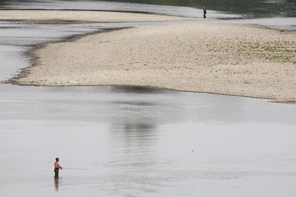 People fish near a hydroelectric power plant at Isola Serafini, on the Po river in San Nazzaro, Italy, Wednesday, June 15, 2022. The drying up of the river is jeopardizing drinking water in Italy's densely populated and highly industrialized districts and threatening irrigation in the most intensively farmed part of the country. (AP Photo/Luca Bruno)