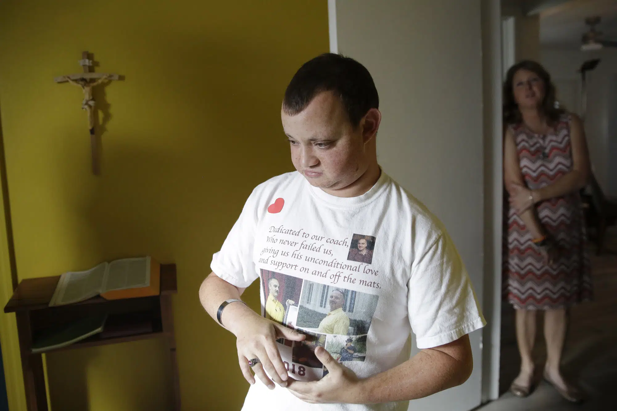 FILE - Corey Hixon, 24, wears a shirt with photographs of his father, Chris Hixon, as his mother, Debbi Hixon, stands in the doorway on Friday, Feb. 14, 2020, in Hollywood, Fla. Chris Hixon was killed in the school shooting on Valentine's Day two years ago at Marjory Stoneman Douglas High School in Parkland, Fla. (AP Photo/Brynn Anderson, File)