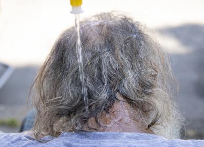 Maggy Johnston, ARCHES outreach coordinator, squeezes water on a man's head during a heat wave with temperatures reaching 100 degrees in Salem, Ore., Tuesday, July 26, 2022. (Brian Hayes/Statesman-Journal via AP)