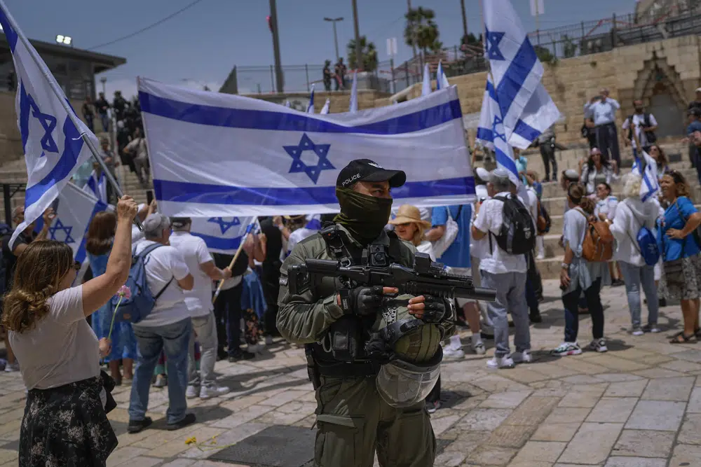 Un agente de la policía de Israel hace guardia mientras israelíes ondean banderas nacionales antes de una marcha por el Día de Jerusalén, un feriado israelí que conmemora la captura de Jerusalén Este en la Guerra de los Seis días en 1967, frente a la Puerta de Damasco de la Ciudad Vieja, en Jerusalén, el 18 de mayo de 2023. (AP Foto/Ohad Zwigenberg)