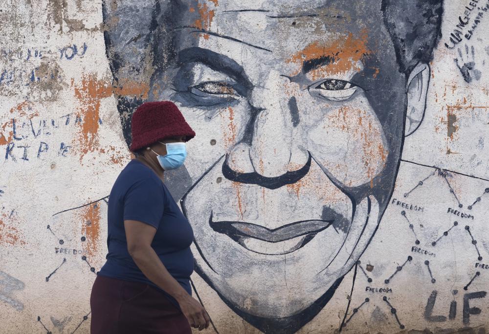 A woman wearing a mask walks past a mural of former South Africa's president Nelson Mandela, in Katlehong, east of Johannesburg, South Africa, Friday, April 29, 2022. South Africa's health minister says it is likely the country has entered a new wave of COVID-19 earlier than expected as new infections and hospitalizations have risen rapidly over the past two weeks. (AP Photo/Themba Hadebe)