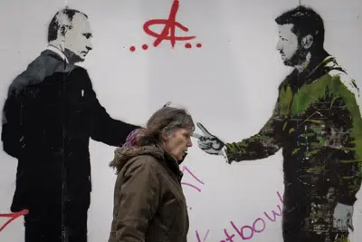 Una mujer camina junto a un graffiti que representa al presidente ucraniano Volodymyr Zelenskyy, a la derecha, y al presidente ruso Vladimir Putin en el centro de Londres, el jueves 4 de mayo de 2023. (AP Photo/Vadim Ghirda)