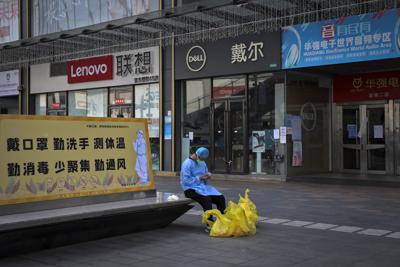 Un hombre con una máscara facial navega por su teléfono inteligente mientras descansa en un banco que muestra un cartel de prevención del coronavirus cerca de las tiendas cerradas en el área de Huaqiangbei, el mercado de electrónica más grande del mundo, en Shenzhen, en la provincia de Guangdong, en el sur de China, el 14 de marzo de 2022. Las empresas en Shenzhen, un importante centro de negocios chino, podrán reabrir mientras avanzan los esfuerzos para contener los brotes de coronavirus, dijo el gobierno el jueves 17 de marzo de 2022 después de un cierre en toda la ciudad que sacudió los mercados financieros. (Chinatopix vía AP)