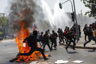 Manifestantes huyen de los cañones de agua de la policía en el tercer aniversario del inicio de las protestas antigubernamentales contra la desigualdad, en Santiago, Chile, el martes 18 de octubre de 2022. (AP Foto/Cristobal Escobar)