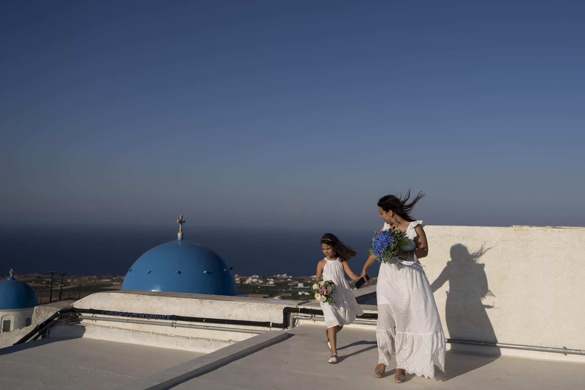 Cinzia Sansone y su hija Josephine, de Trieste, Italia, posan para fotos en una azotea con vista al Monasterio Católico de Santa Catalina en la isla griega de Santorini el martes, 14 de junio de 2022. (Foto AP/Petros Giannakouris)