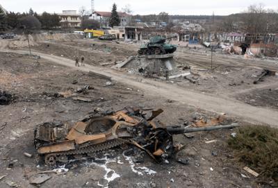 Local residents pass at a damaged Russian tank in the town of Trostsyanets, some 400km (250 miles) east of capital Kyiv, Ukraine, Monday, March 28, 2022. The monument to Second World War is seen in background. The more than month-old war has killed thousands and driven more than 10 million Ukrainians from their homes including almost 4 million from their country. (AP Photo/Efrem Lukatsky)