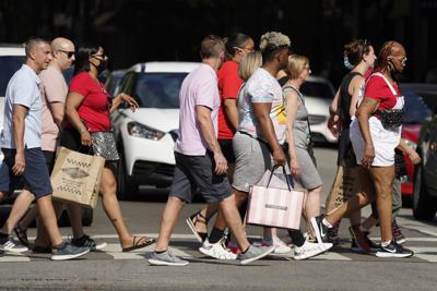 Personas cruzan la calle en el centro de Chicago con sus bolsas de compra, el sábado 22 de mayo de 2021. (AP Foto/Nam Y. Huh)
