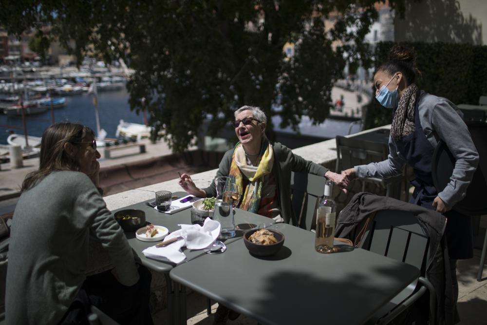 FILE - In this May 19, 2021, file photo, Dany Barrau reacts with a waitress after being served, at a restaurant terrace in La Ciotat southern France. Coronavirus infections, hospitalizations and deaths are plummeting across much of Europe. Vaccination rates are accelerating, and with them, the promise of summer vacations. (AP Photo/Daniel Cole, File)