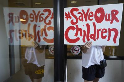 Un manifestante sostiene una pancarta frente a las ventanas de la oficina central del distrito escolar unificado de Los Ángeles, el jueves 9 de septiembre de 2021, en Los Ángeles. (AP Foto/Damian Dovarganes)