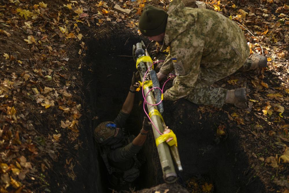 Desminadores de las fuerzas de defensa territorial de Ucrania colocan armas y munición rusa en un hoyo para su destrucción, durante una operación de desminado cerca de Hrakove, Ucrania, el 13 de octubre de 2022. (AP Foto/Francisco Seco)