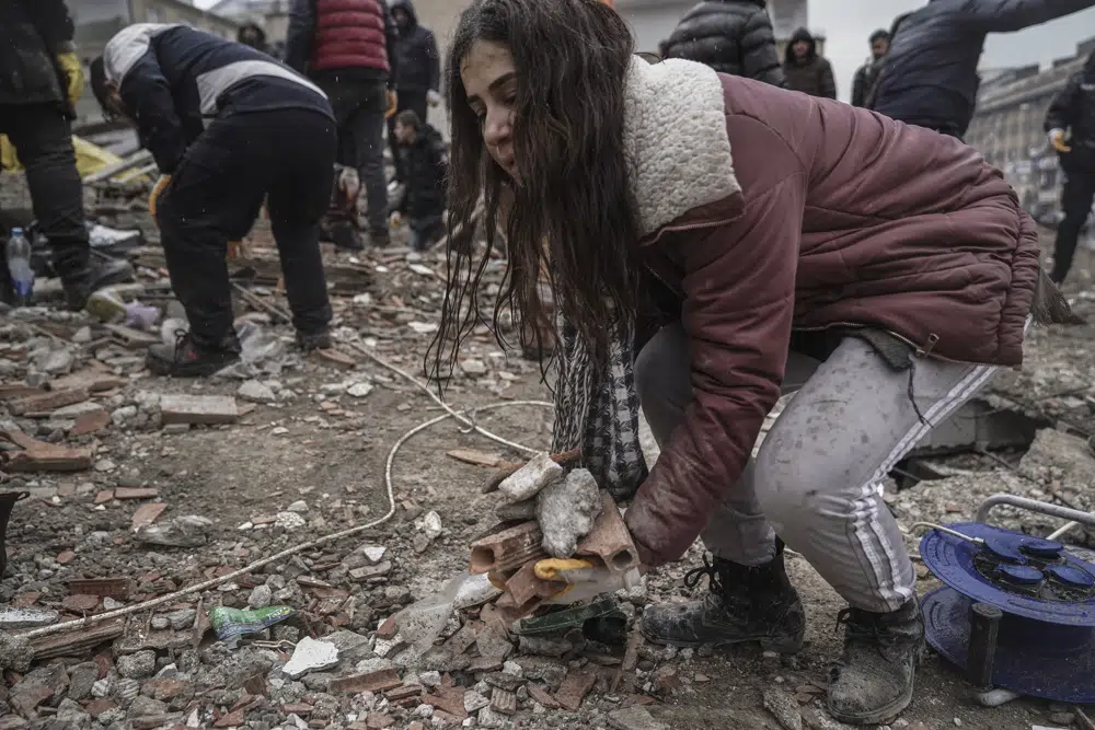 A young women removes debris from a destroyed building as she searches for people with emergency teams in Gaziantep, Turkey, Monday, Feb. 6, 2023. A powerful quake has knocked down multiple buildings in southeast Turkey and Syria and many casualties are feared. (AP Photo/Mustafa Karali)