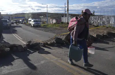 Una mujer cargada con contenedores llenos de leche atraviesa caminando los bloqueos de carretera colocados por los manifestantes de oposición al gobierno en la carretera de Juliaca a Puno, Bolivia, el viernes 10 de marzo de 2023. Las protestas exigen un adelanto electoral inmediato, la renuncia de la presidenta peruana, Dina Boluarte, y del Congreso, que destituyó al expresidente, ahora en prisión preventiva, por intentar disolver el Parlamento en diciembre para evitar su remoción del cargo. (AP Foto/Juan Karita)