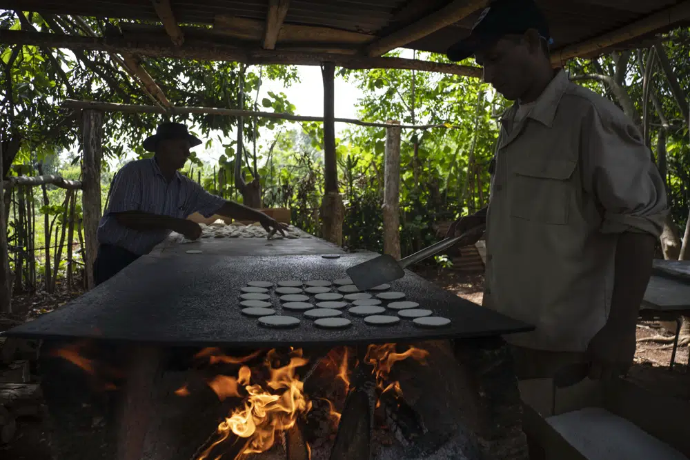 El productor de casabe Julio César Núnez, a la izquierda, y su sobrino Agustín cocinan pequeñas tortillas de casabe una plancha al fuego de leña, en Quivicán, Cuba, el lunes 28 de mayo de 2023. Cuando Núñez, de 80 años, era niño ayudaba a su abuela a rallar la yuca, utilizando herramientas artesanales -y un antiguo método de preparación- para convertir la yuca rallada en una tortilla delgada, blanca y crujiente. (AP Foto/Ramón Espinosa)