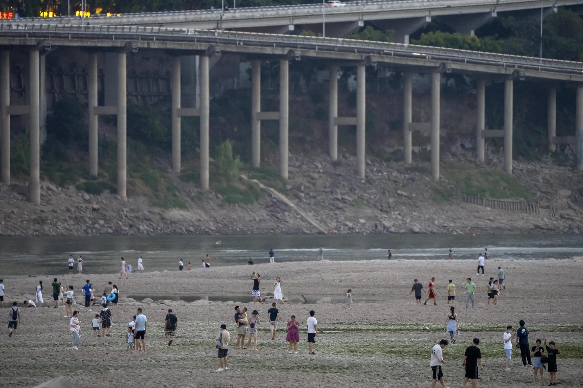 People walk along the dry riverbed of the Jialing River, a tributary of the Yangtze, in southwestern China's Chongqing Municipality, Saturday, Aug. 20, 2022. The very landscape of Chongqing, a megacity on the Yangtze River, has been transformed by China's worst heat wave since modern record-keeping began six decades ago, and an accompanying drought. (AP Photo/Mark Schiefelbein)