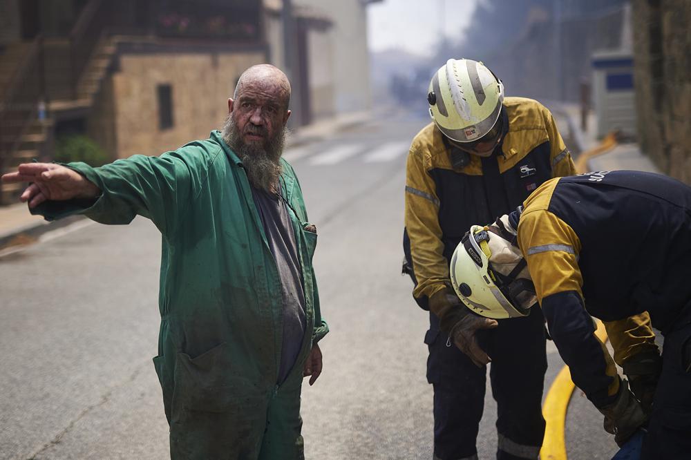 A neighbour helps firefighters in San Martin de Unx in northern Spain, Sunday, June 19, 2022. Firefighters in Spain are struggling to contain wildfires in several parts of the country which as been suffering an unusual heat wave for this time of the year. (AP Photo/Miguel Oses)