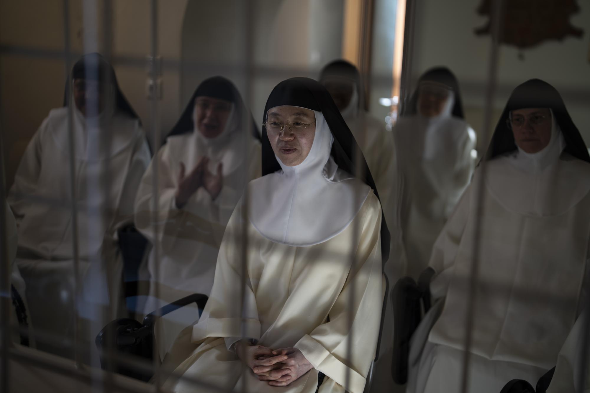 La hermana María de la Trinidad, al centro, y otras monjas de clausura hablan con los periodistas desde detrás de una reja de hierro blanco en el salón del Monasterio de Santa Catalina en la isla griega de Santorini el martes 14 de junio de 2022. El convento alberga a más de una decena de monjas que se dedican a la oración y salen sólo por necesidades médicas o gubernamentales.  (Foto AP/Petros Giannakouris)